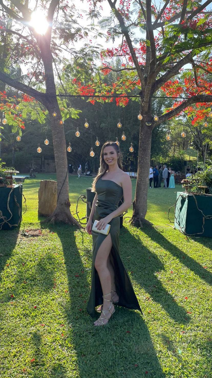 Vestido longo verde oliva em tecido acetinado, decote de um ombro só, modelagem reta e fenda lateral profunda.
