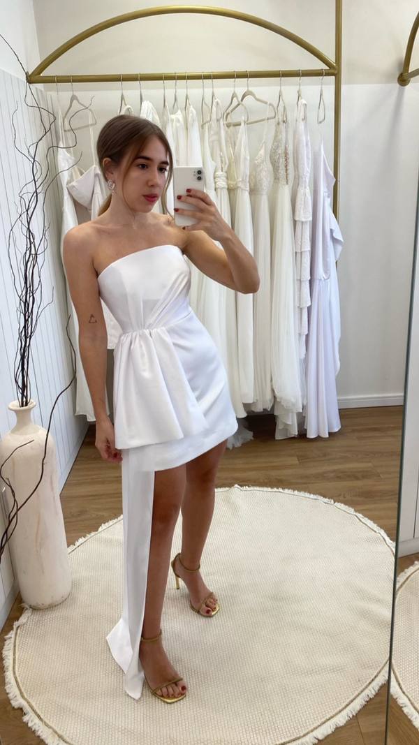 Vestido curto branco tomara que caia com efeito drapeado na cintura e cauda lateral.