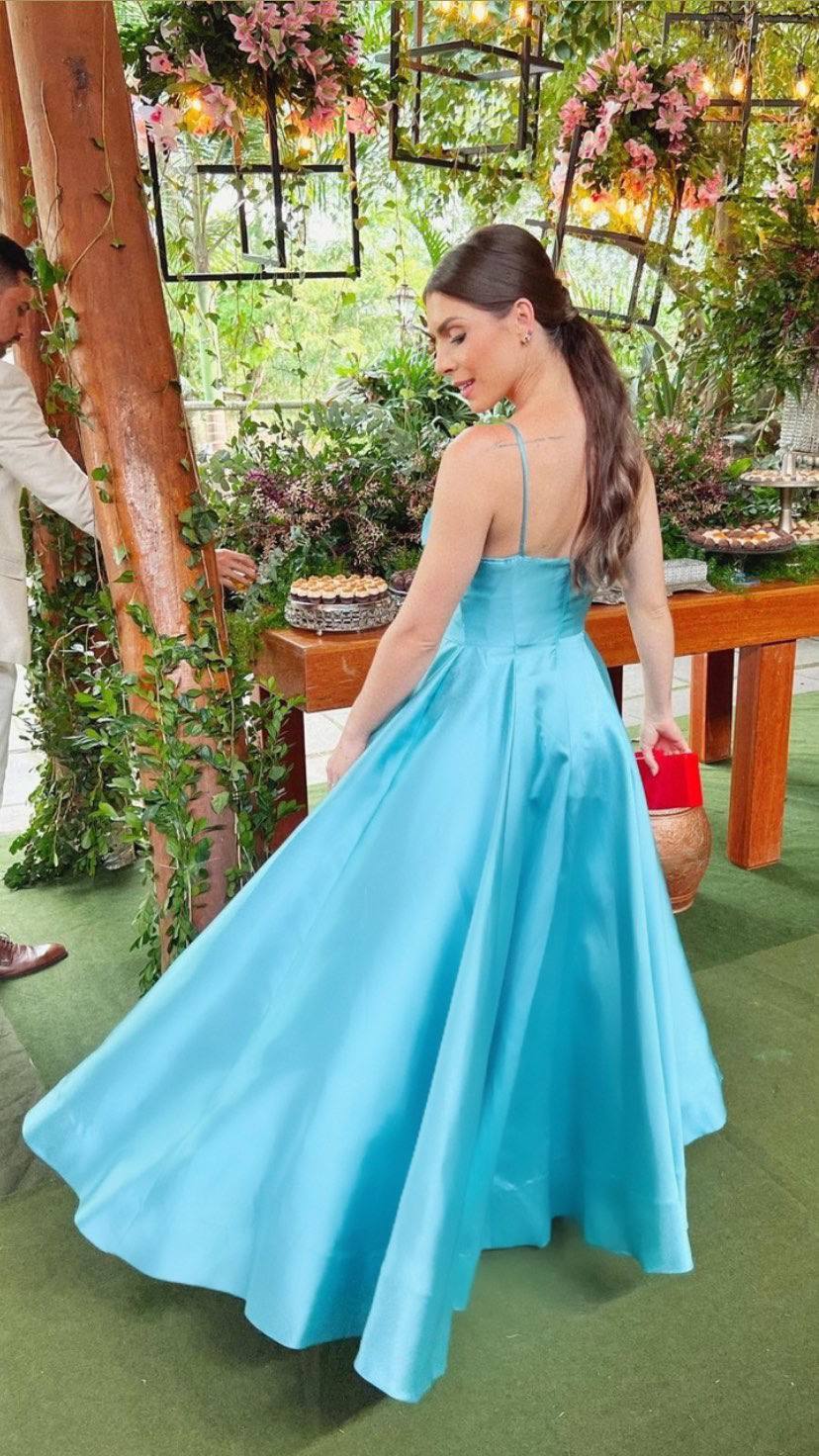 Vestido longo azul claro em tecido acetinado, com alças finas, cintura marcada e saia evasê volumosa.