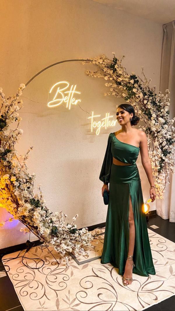 Vestido longo verde de cetim, modelo um ombro com uma manga longa, recorte na cintura e fenda na saia.