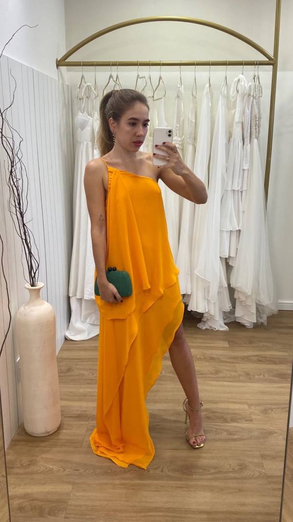 Vestido longo laranja de caimento fluido, decote um ombro, camadas em barra assimétrica e fenda lateral.