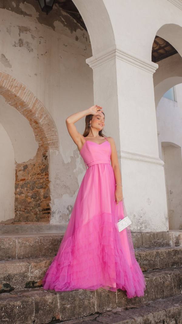 Vestido longo rosa fúcsia de alça fina, feito em tule com saia de babados e cintura marcada.