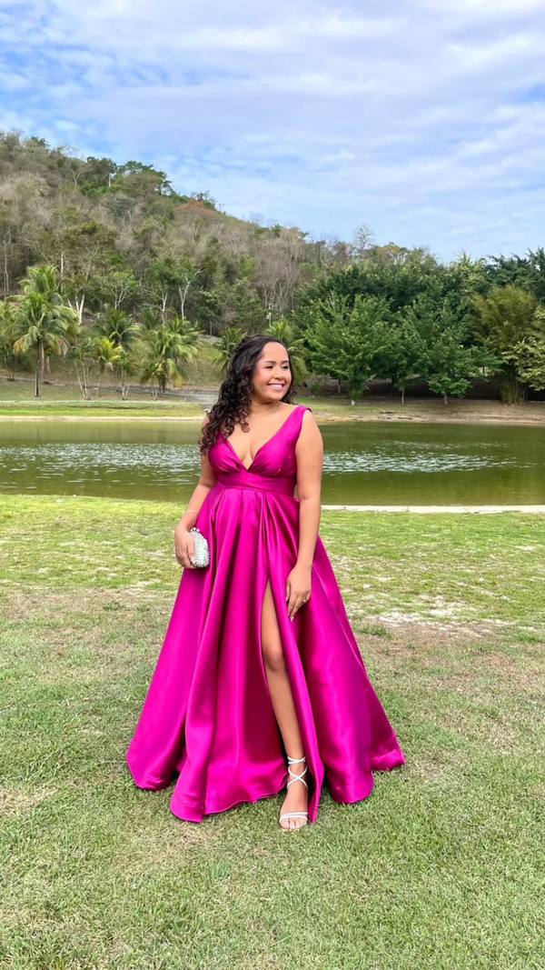 Vestido longo fúcsia em tecido acetinado, com decote V, saia ampla e fenda lateral em destaque.