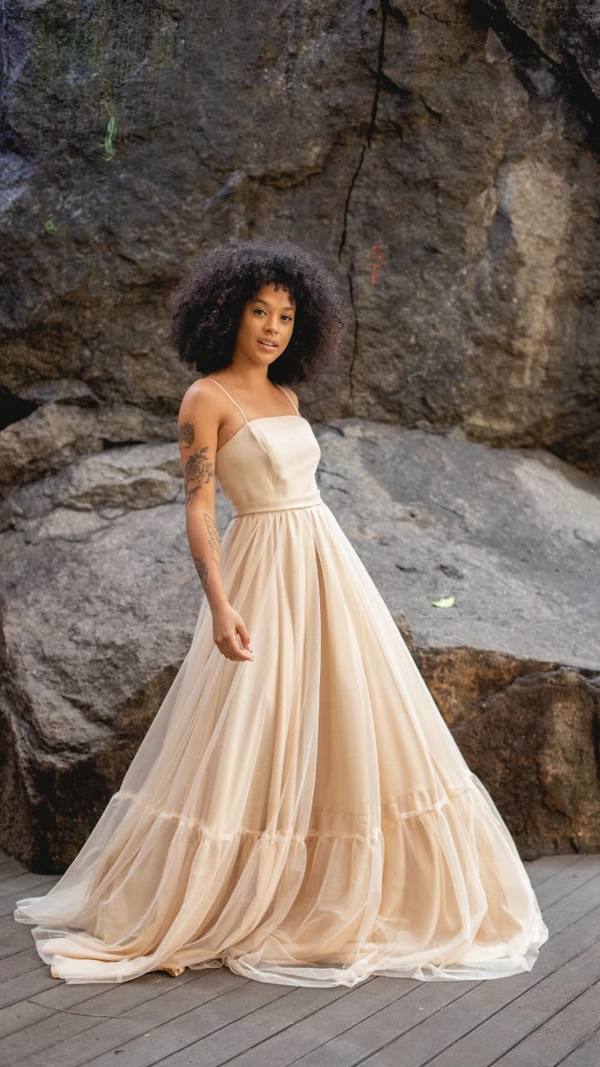 Vestido longo de tule bege com alças finas, decote reto e saia volumosa em camadas.