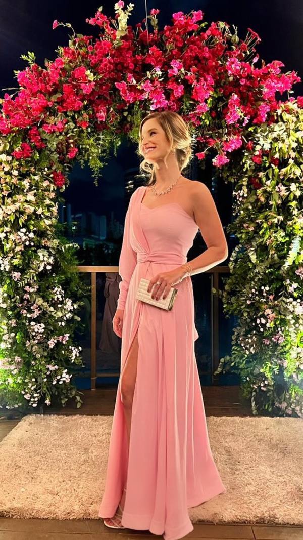 Vestido longo rosa em tecido fluido, modelo um ombro só com manga longa, detalhe drapeado na cintura e fenda lateral.