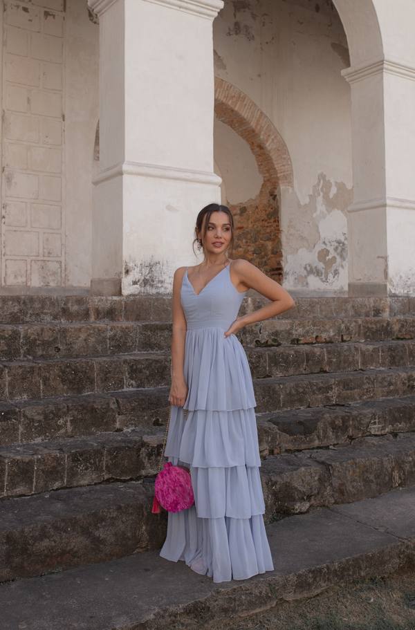 Vestido longo azul claro de tecido fluido, com alças finas, decote V e saia em camadas sobrepostas.