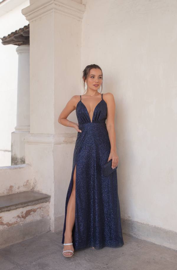 Vestido longo azul escuro com brilho, alças finas, decote V profundo e fenda lateral na saia.