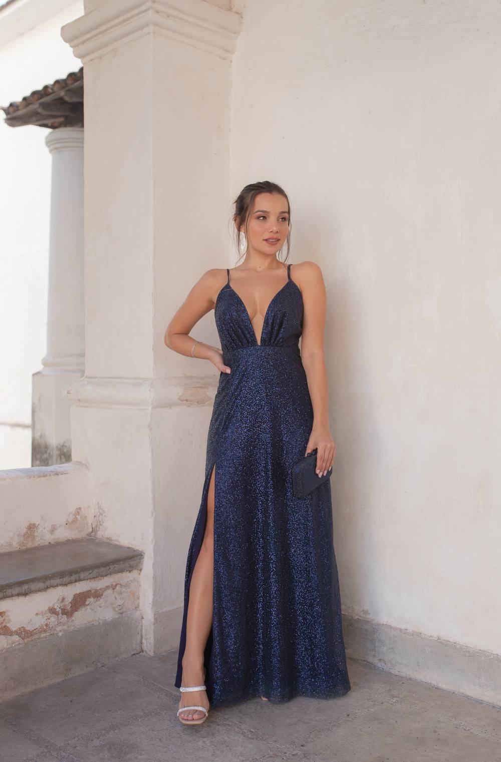 Vestido longo azul escuro com brilho, alças finas, decote V profundo e fenda lateral na saia.
