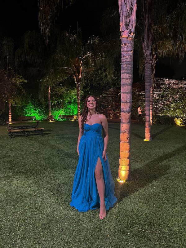 Vestido longo azul com decote tomara que caia, saia fluida com fenda alta e leve brilho no tecido.