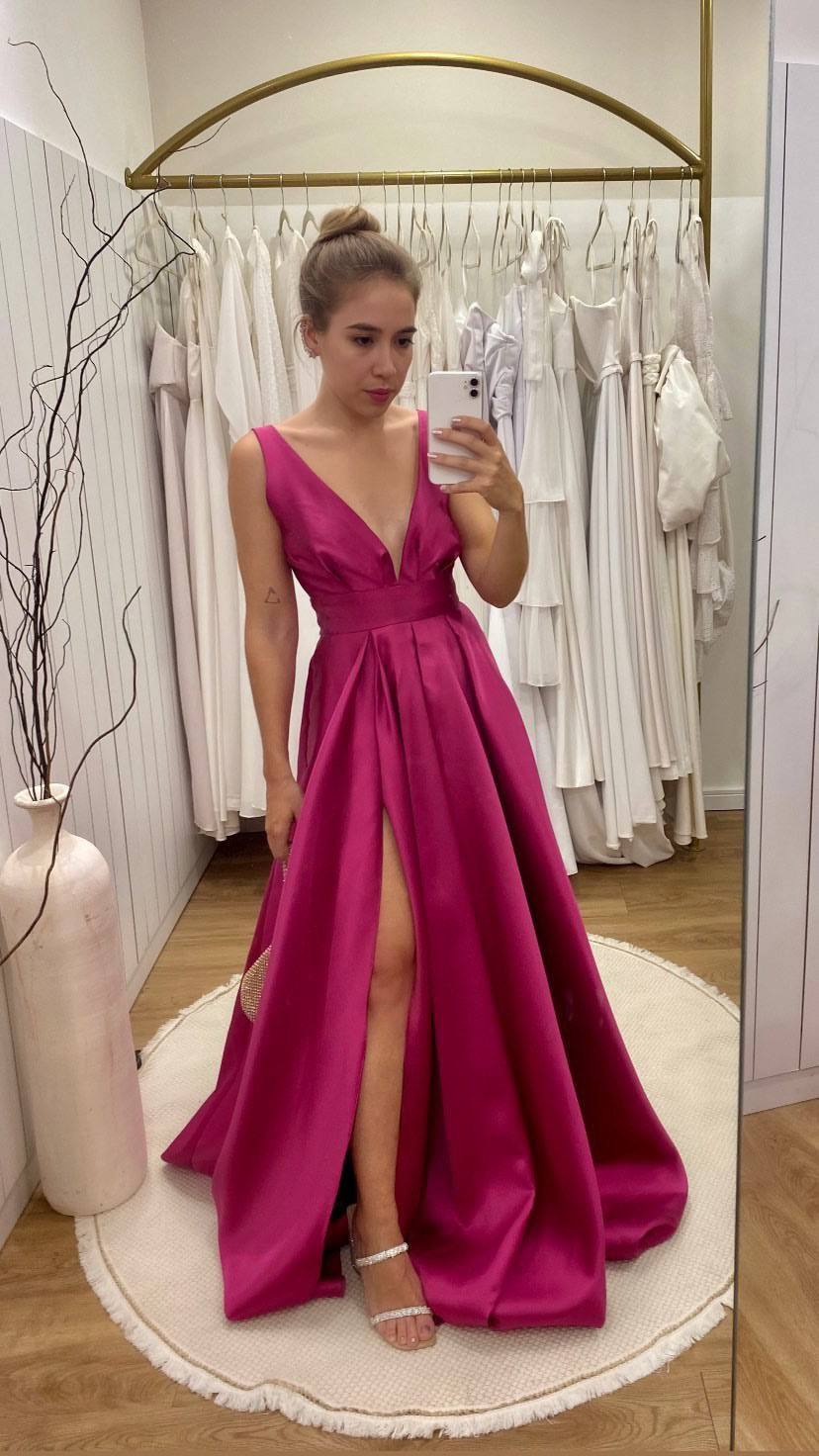 Vestido longo fúcsia acinturado com decote V profundo, saia rodada com fenda frontal e pregas.